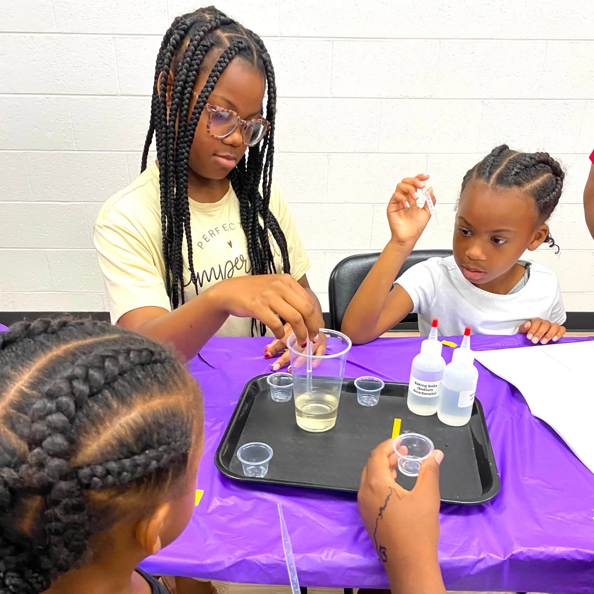 Three girls doing a science experiment with liquid and test strips.